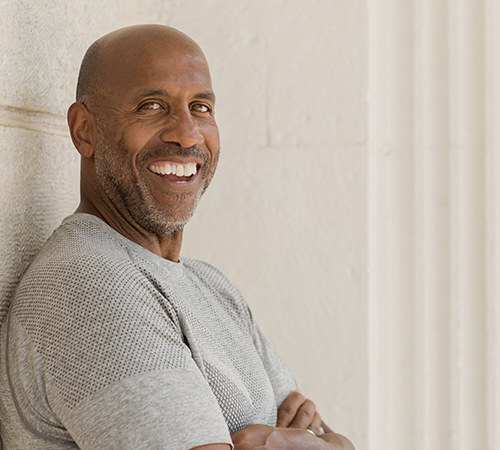 smiling man leaning against wall with arms folded